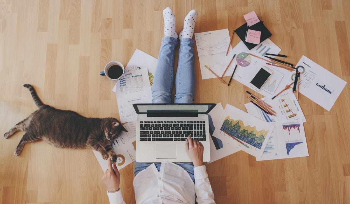 person sat on the floor using a laptop with notes scattered around the room