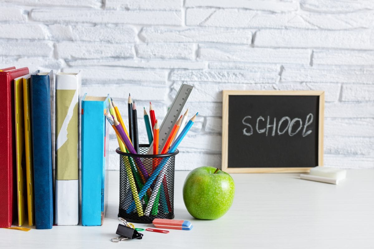 school sign on a desk next to books and coloured pencils